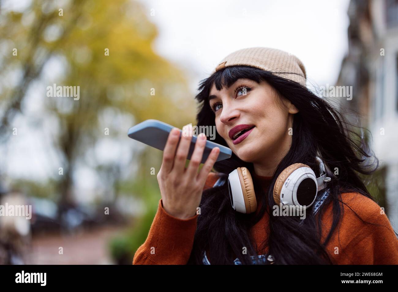 Bella donna felice che indossa un cappello in maglia e invia messaggi vocali tramite smartphone Foto Stock