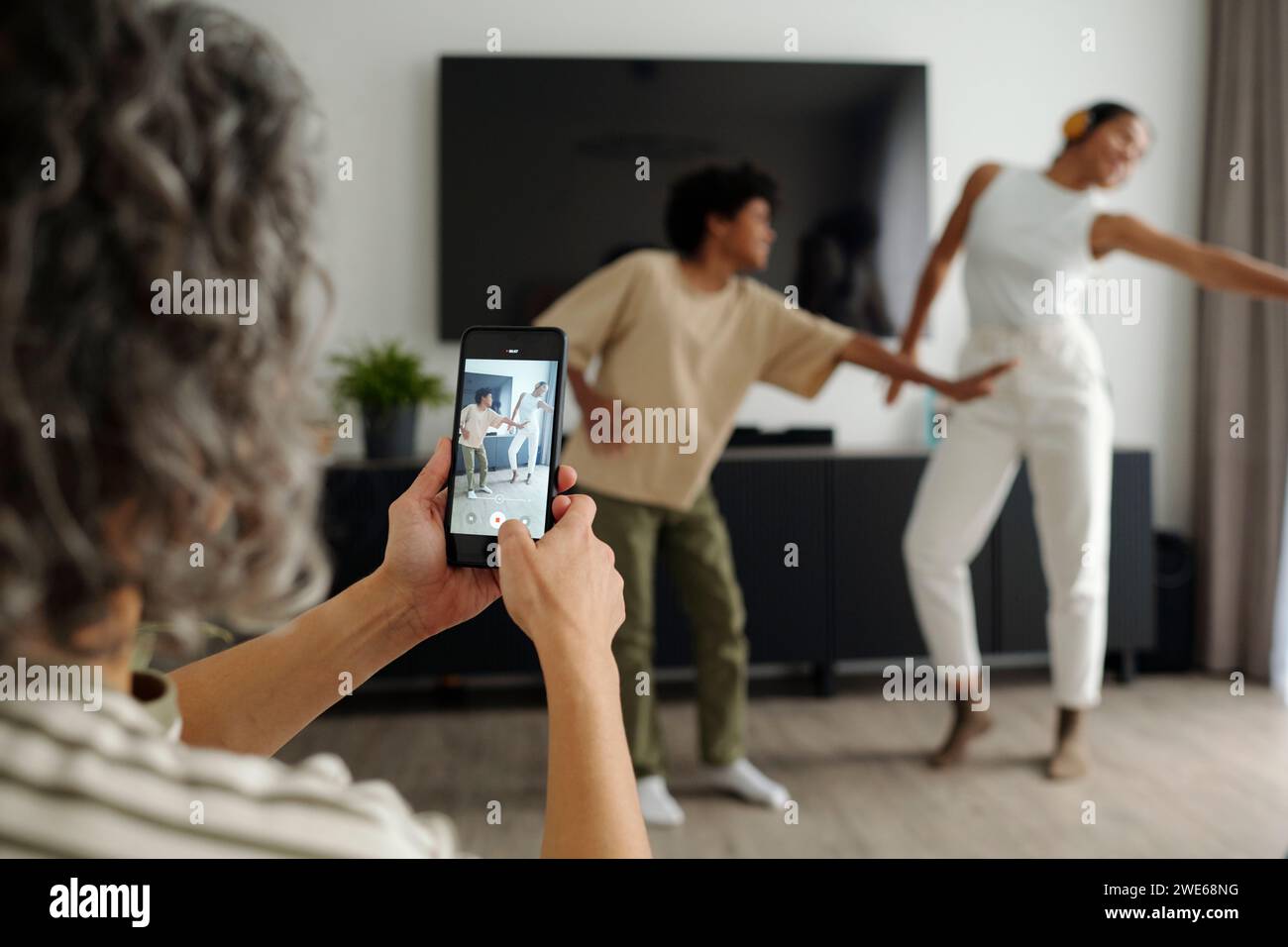 Madre che usa uno smartphone e filma video dei suoi figli che ballano a casa Foto Stock