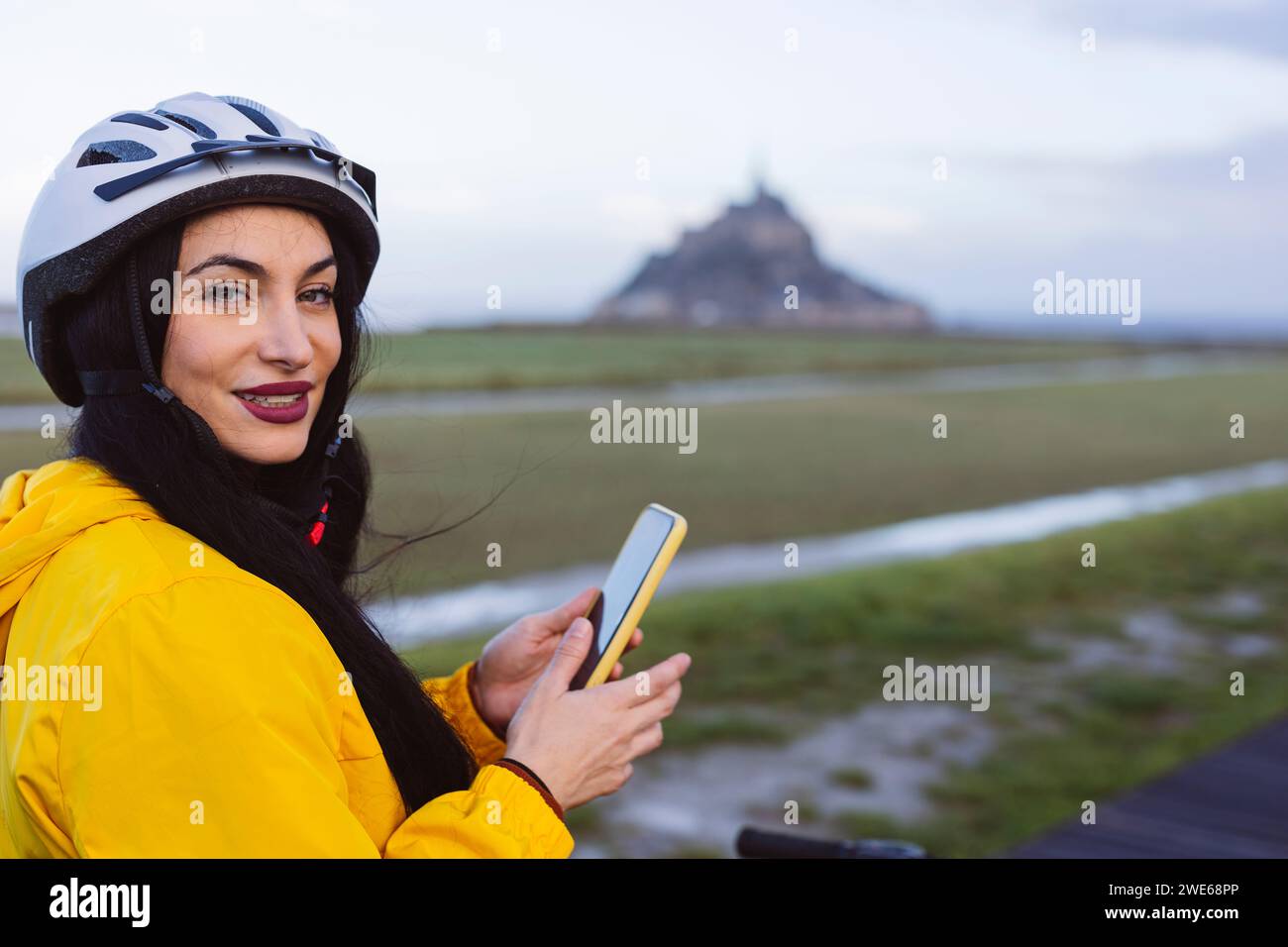 Donna sorridente che indossa un casco da ciclismo con smartphone Foto Stock