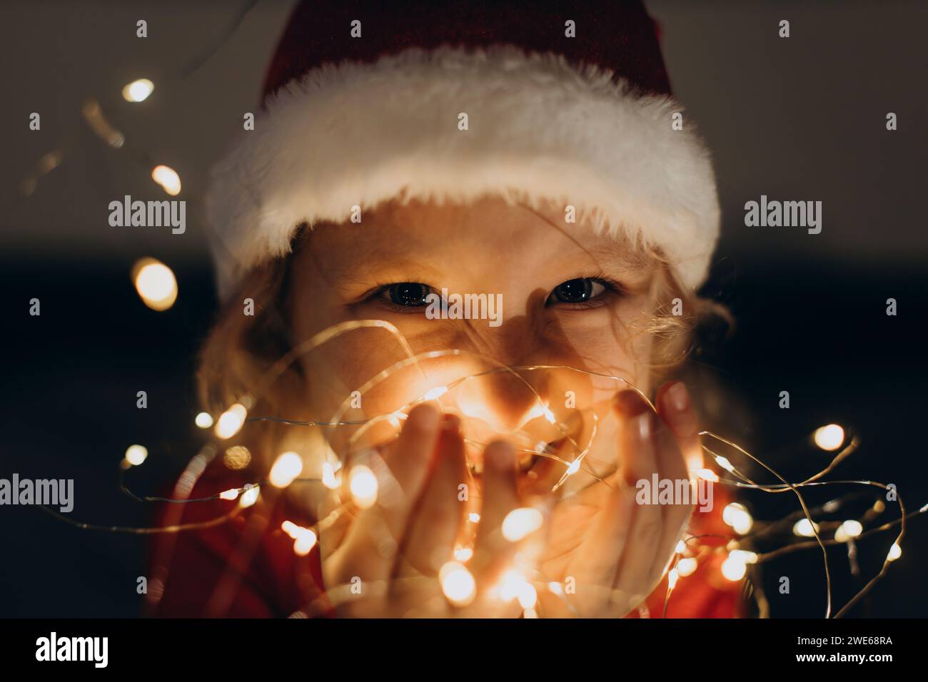 Ragazza felice che indossa il cappello di Babbo Natale e tiene in mano le luci a corda Foto Stock