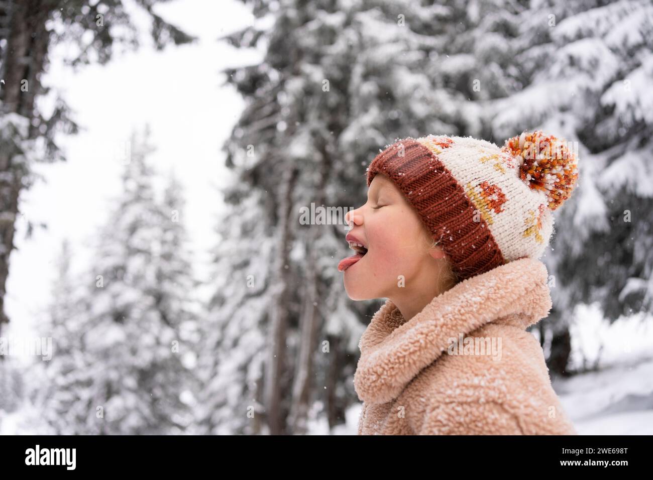 Ragazza felice che si tira fuori la lingua e mangia la neve in inverno Foto Stock