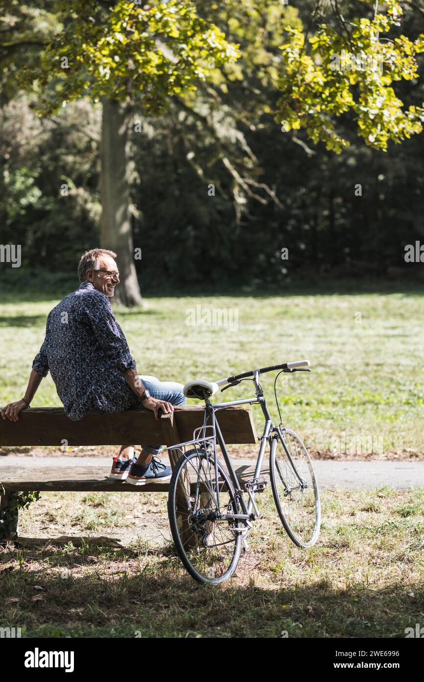 Uomo anziano seduto sulla panchina in bicicletta nel parco nelle giornate di sole Foto Stock