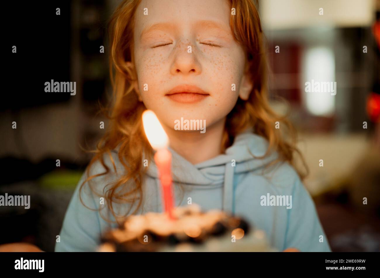 Ragazza che tiene una torta di compleanno con una candela a casa Foto Stock