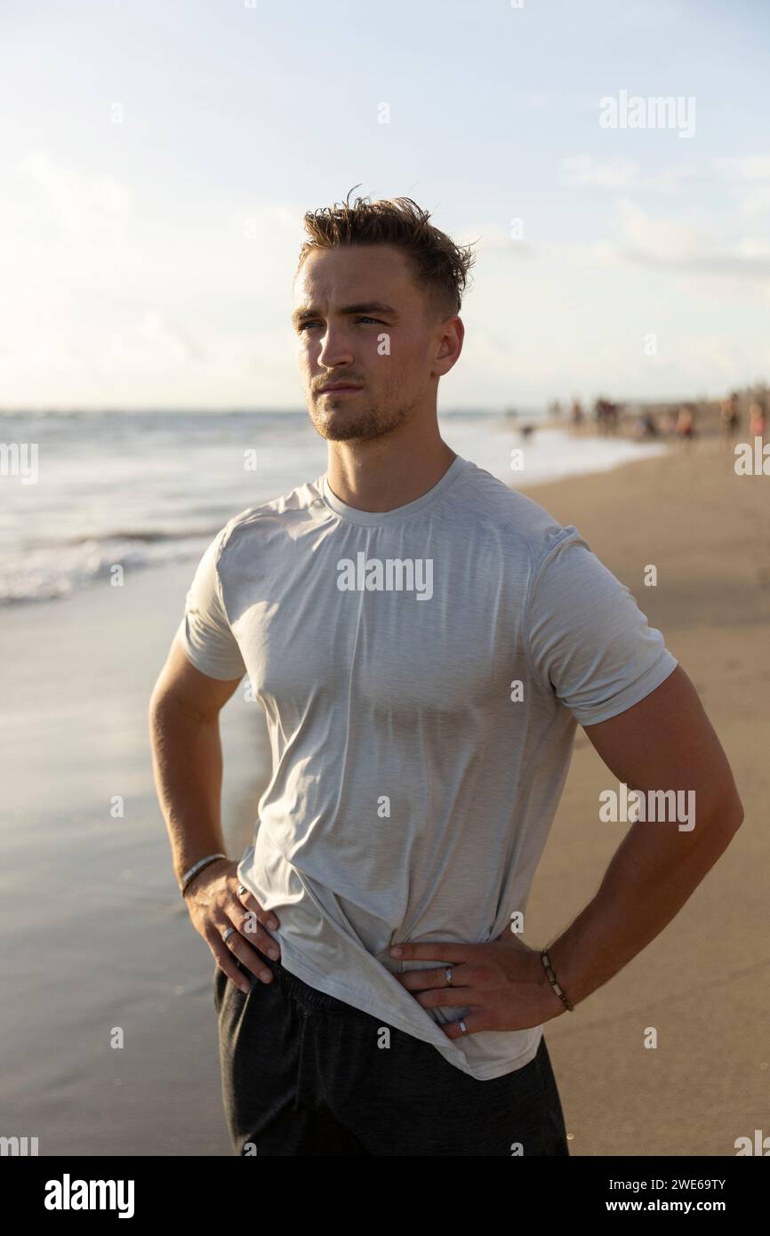 Giovane uomo in piedi con le mani sui fianchi in spiaggia Foto Stock