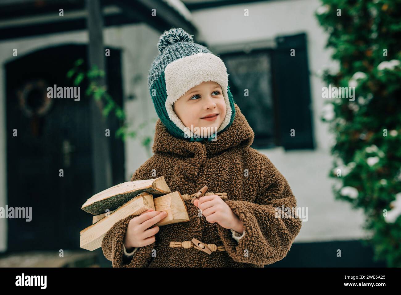 Ragazzo sorridente che indossa abiti caldi e porta legna da ardere Foto Stock