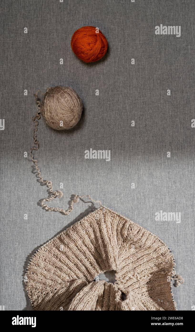 Maglione lavorato a maglia e palle di beige e filato di terracotta sul tavolo su sfondo grigio Foto Stock