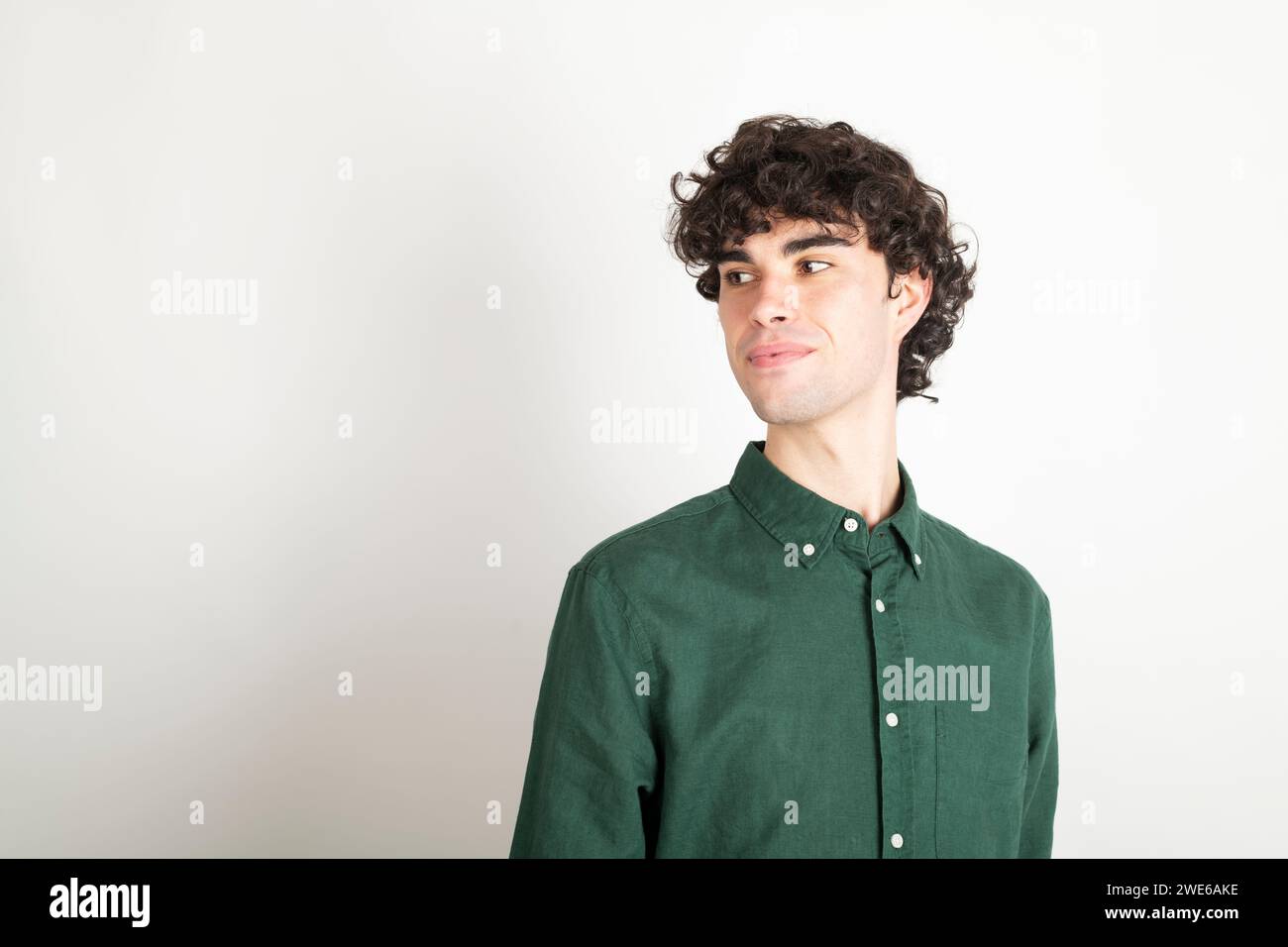 Uomo sorridente con capelli ricci che indossa una camicia verde su sfondo bianco Foto Stock