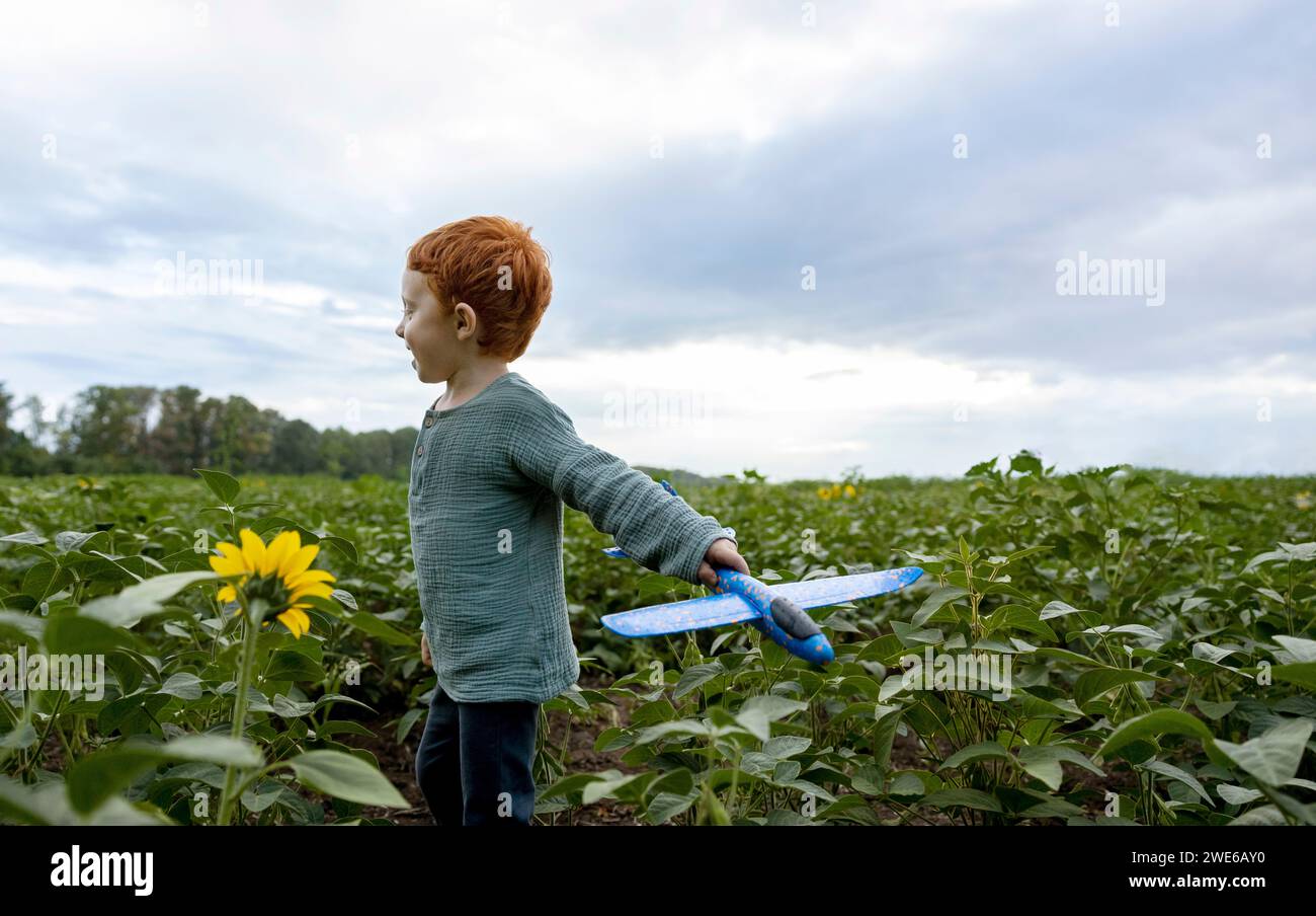 Redhead boy che gioca con l'aereo giocattolo in campo Foto Stock