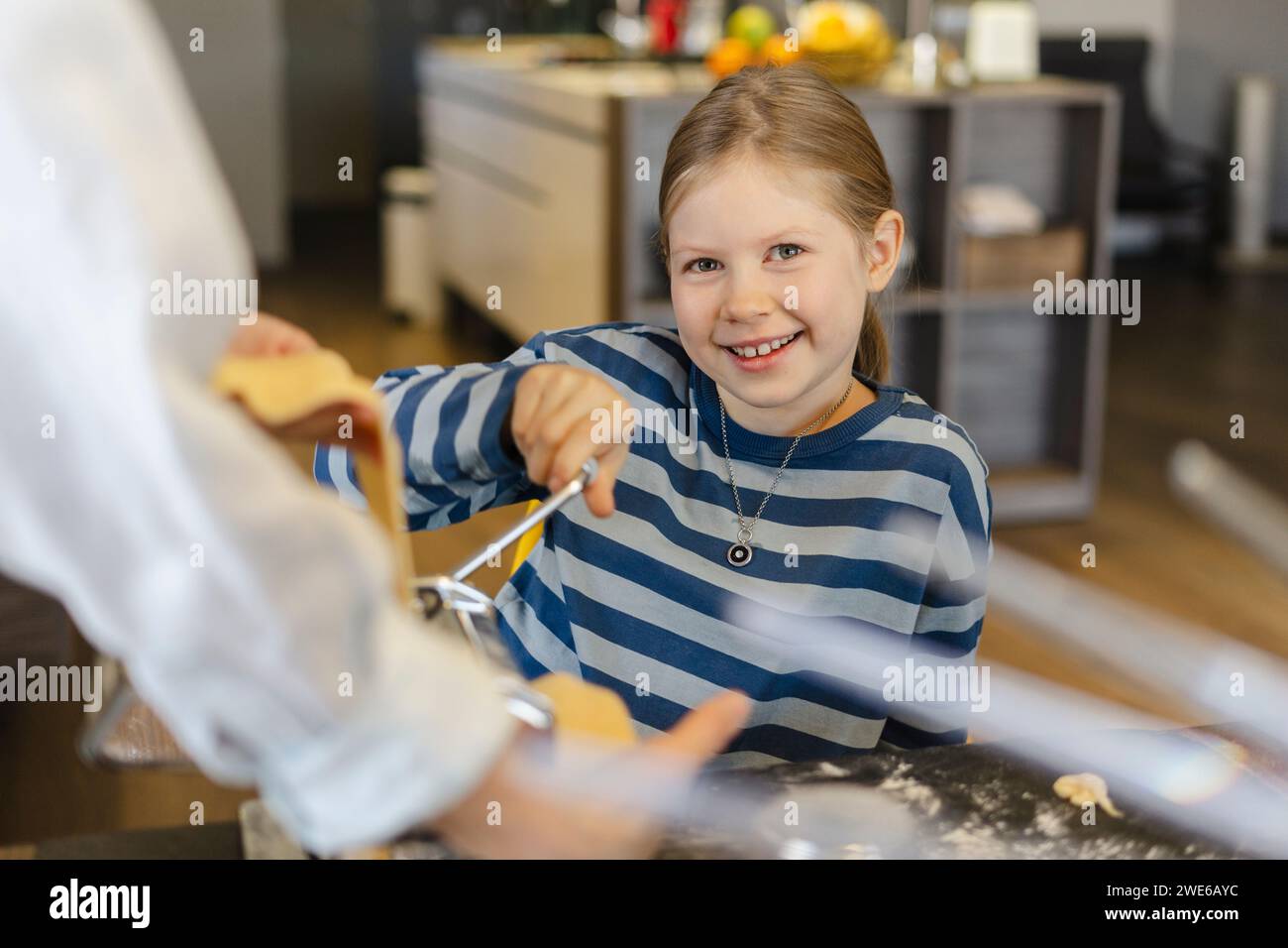 Ragazza felice con la madre che taglia l'impasto nella macchina per la pasta Foto Stock