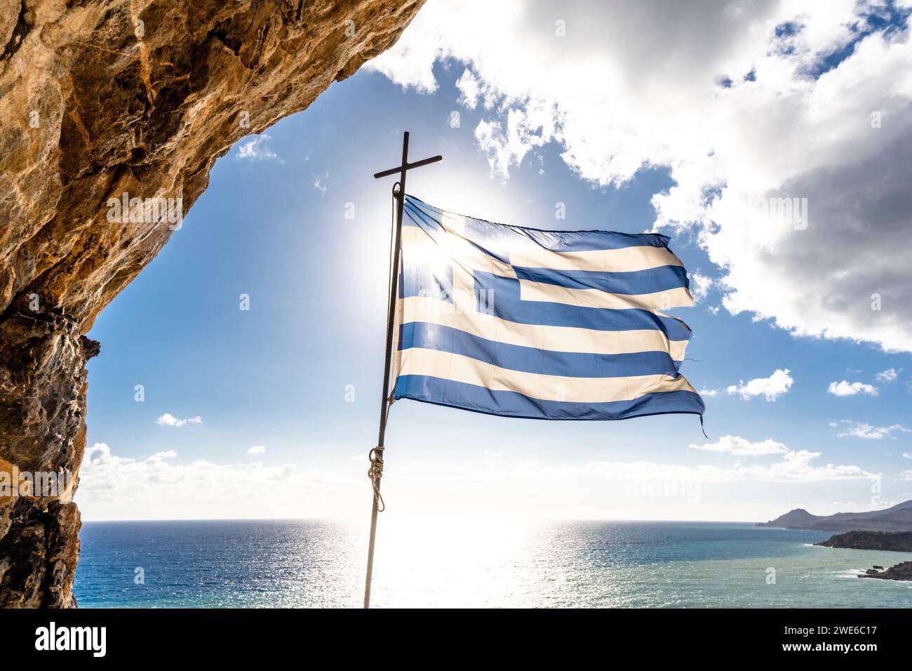 Grecia, Creta, bandiera greca che fluttua contro il sole che splende sul Mar Mediterraneo Foto Stock