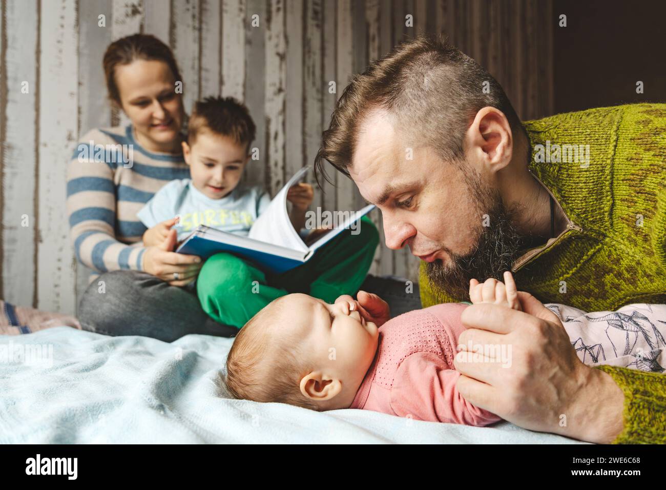 Padre che abbraccia la figlia e la madre che legge un libro con il figlio a casa Foto Stock