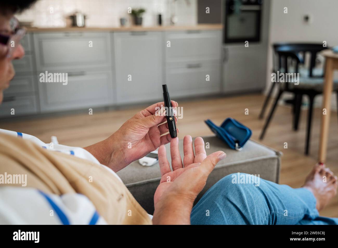 Donna anziana che perfora il dito per l'esame dello zucchero nel sangue a casa Foto Stock