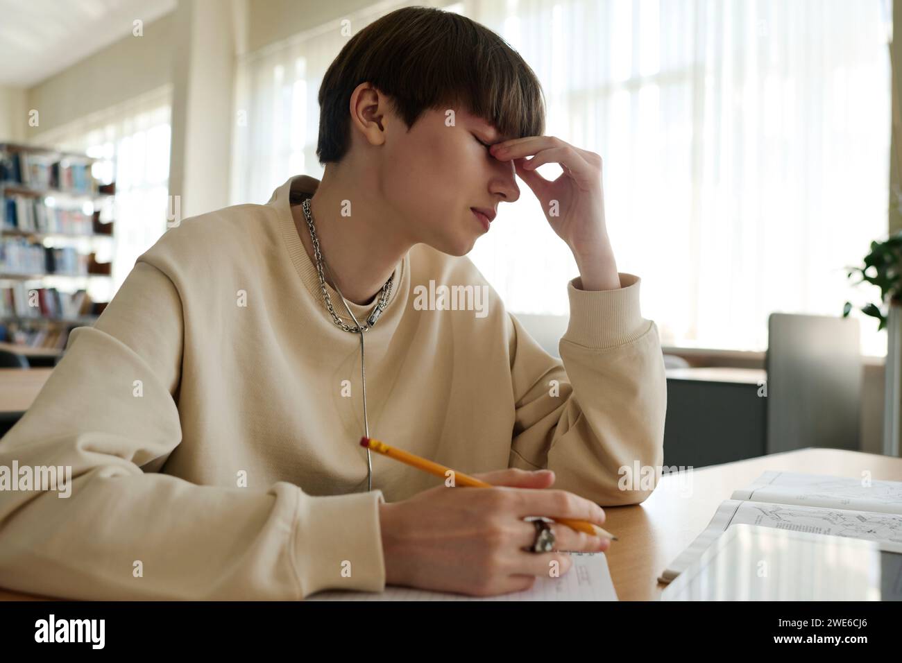 Studente stanco che si strofina gli occhi in biblioteca Foto Stock