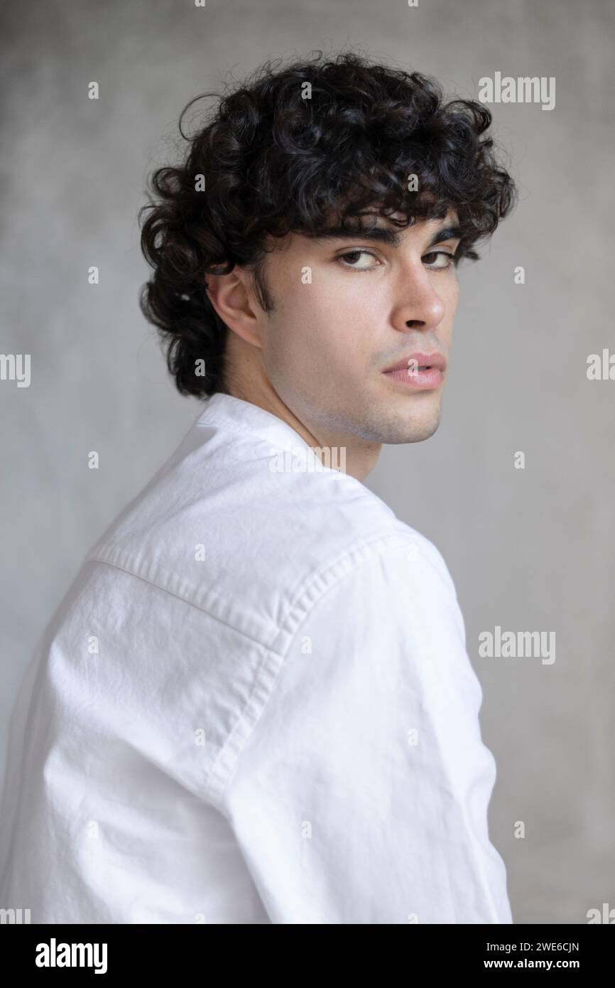 Giovane uomo con capelli ricci che indossa una camicia bianca su sfondo grigio Foto Stock