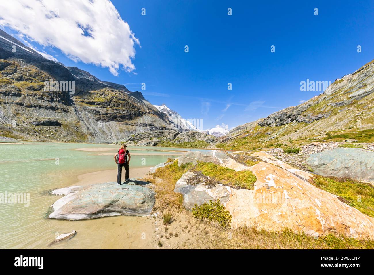 Donna in piedi sulla roccia vicino al lago Sandersee sotto il cielo a Grossglockner, Austria Foto Stock