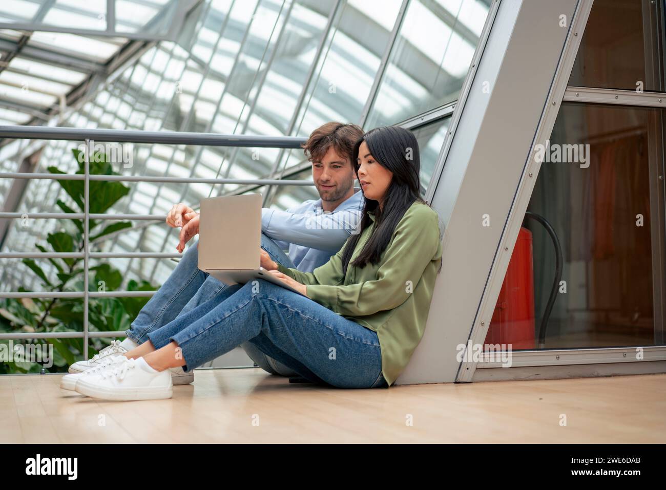 Colleghi multirazziali che utilizzano un computer portatile seduto nel corridoio dell'ufficio Foto Stock