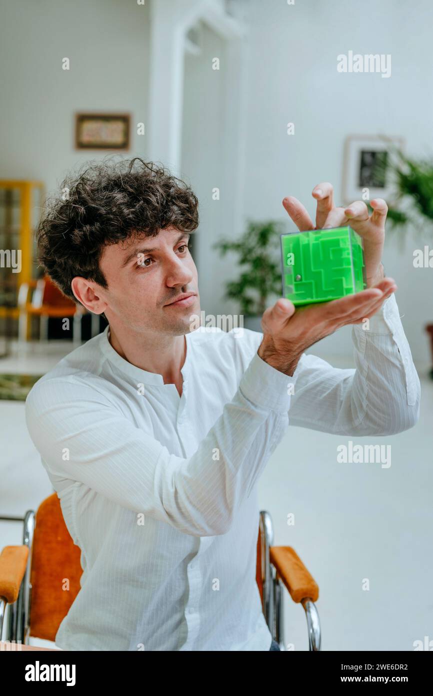 Uomo d'affari che tiene in mano ed esamina il labirinto a forma di cubo in ufficio Foto Stock