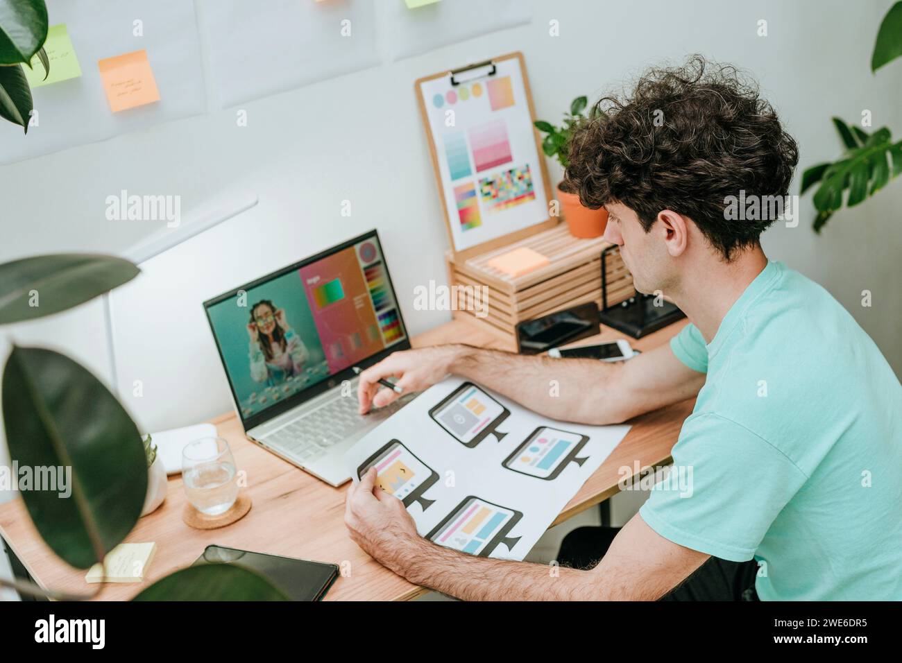 Web designer che tiene un documento e lavora su un computer portatile alla scrivania in ufficio Foto Stock