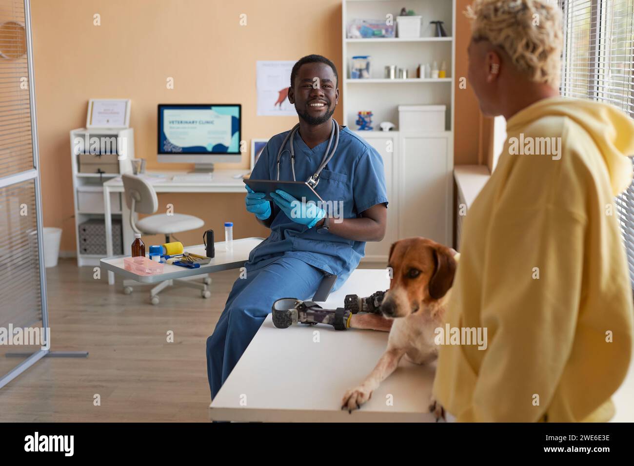 Veterinario felice tenendo tablet PC e discutendo con il proprietario del cane in clinica Foto Stock