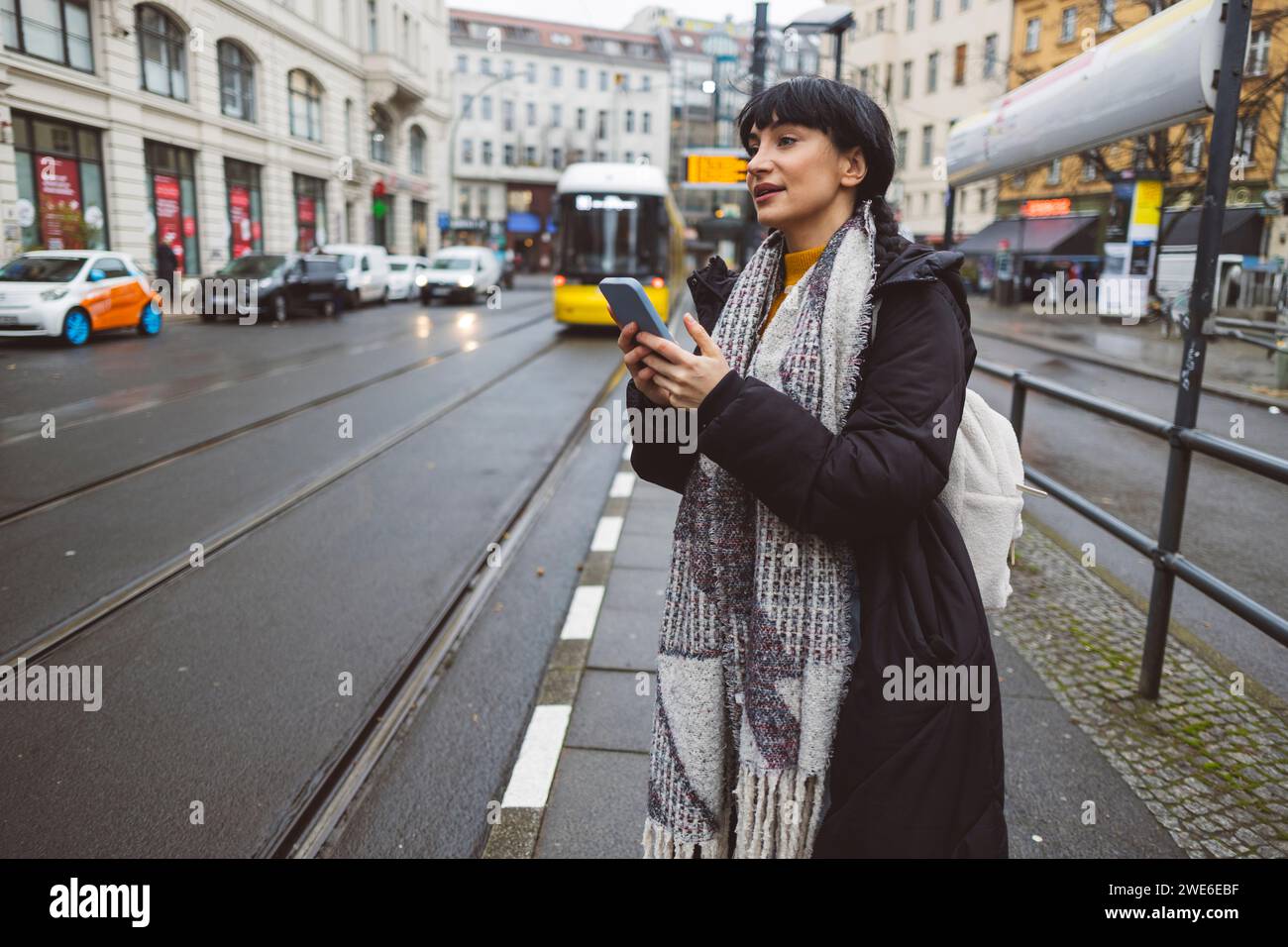 Donna sorridente con smartphone in piedi alla stazione del tram Foto Stock