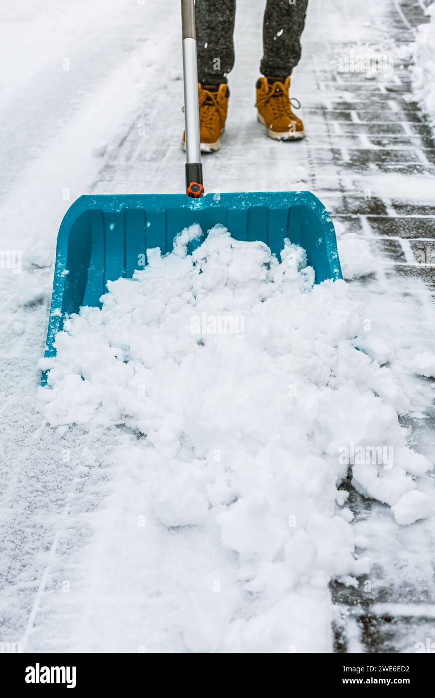 Pulire la neve dalla strada in inverno con una pala dopo una tempesta di neve. Pulizia del marciapiede dalla neve in un giorno d'inverno. Foto Stock