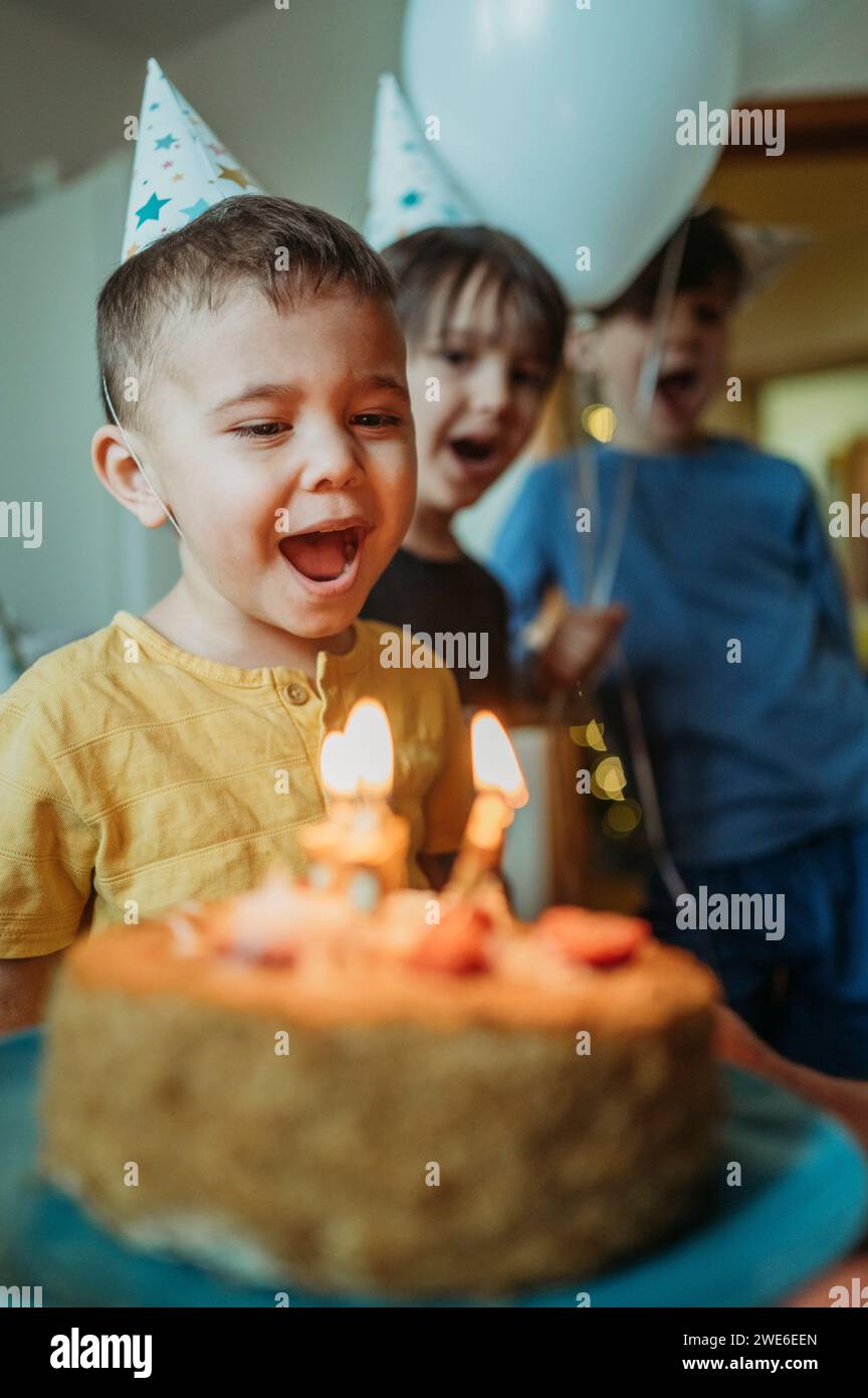 Un ragazzo con le candele di compleanno a bocca aperta sulla torta a casa Foto Stock