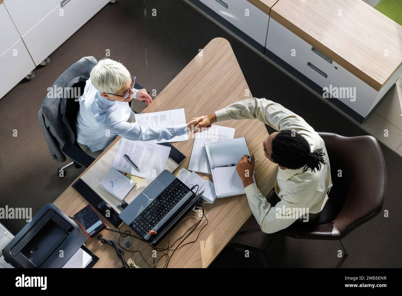 Intervistatore che stringe la mano con il candidato seduto alla scrivania in ufficio Foto Stock