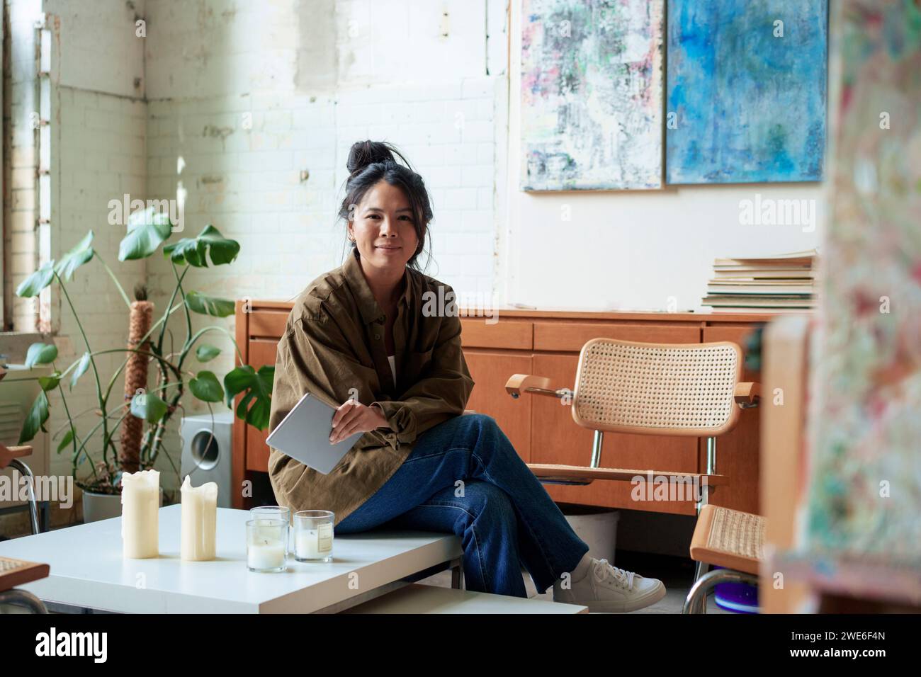 Artista sorridente con tablet PC seduto sul tavolino in officina Foto Stock