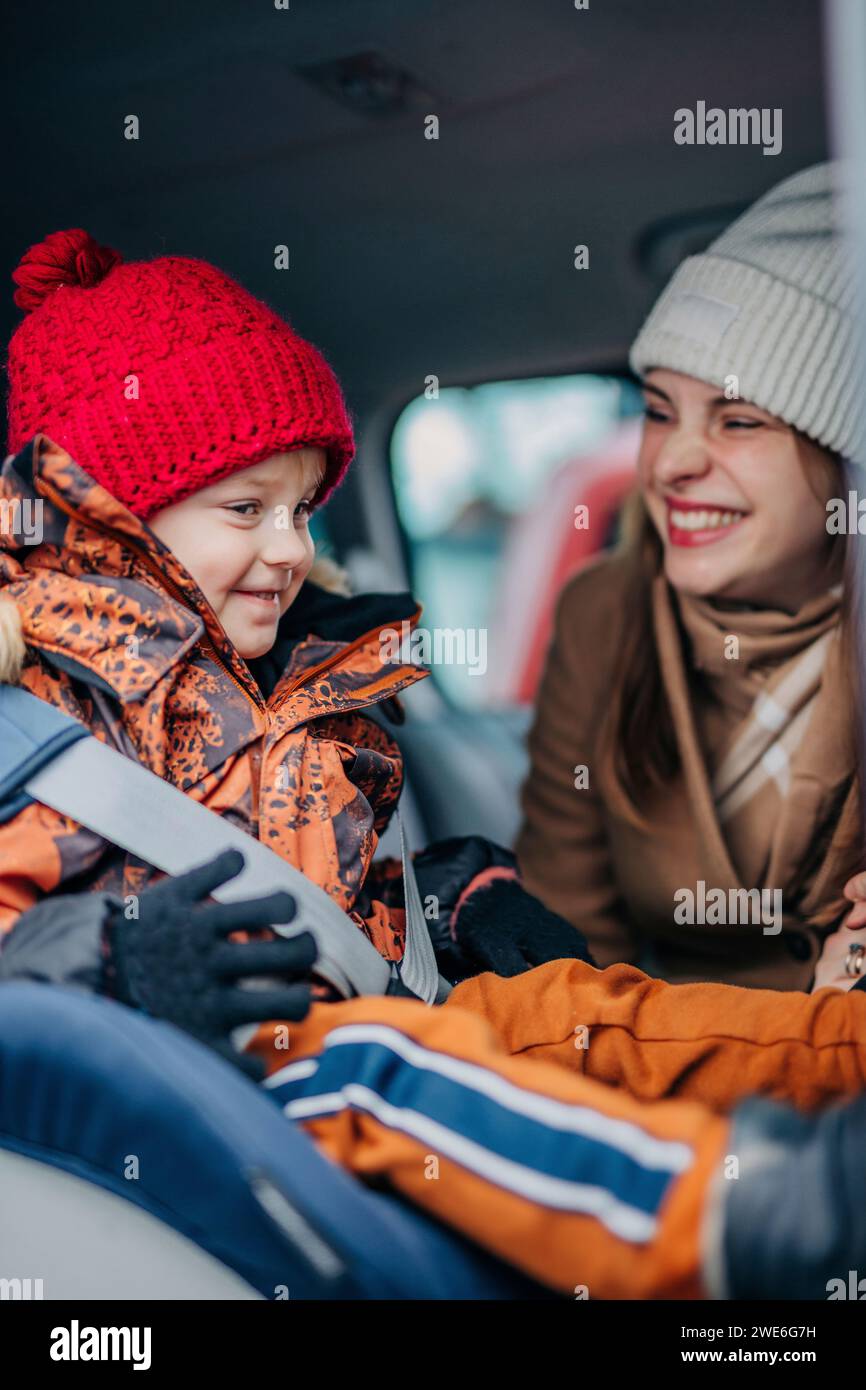 Felice madre che fissa la cintura di sicurezza di auto per figlio Foto Stock