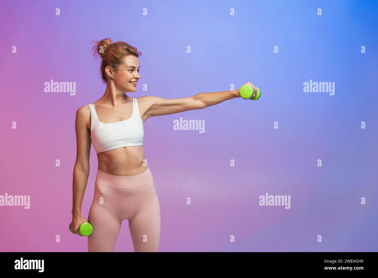 Donna sorridente che si esercita con manubri in piedi su uno sfondo bicolore Foto Stock