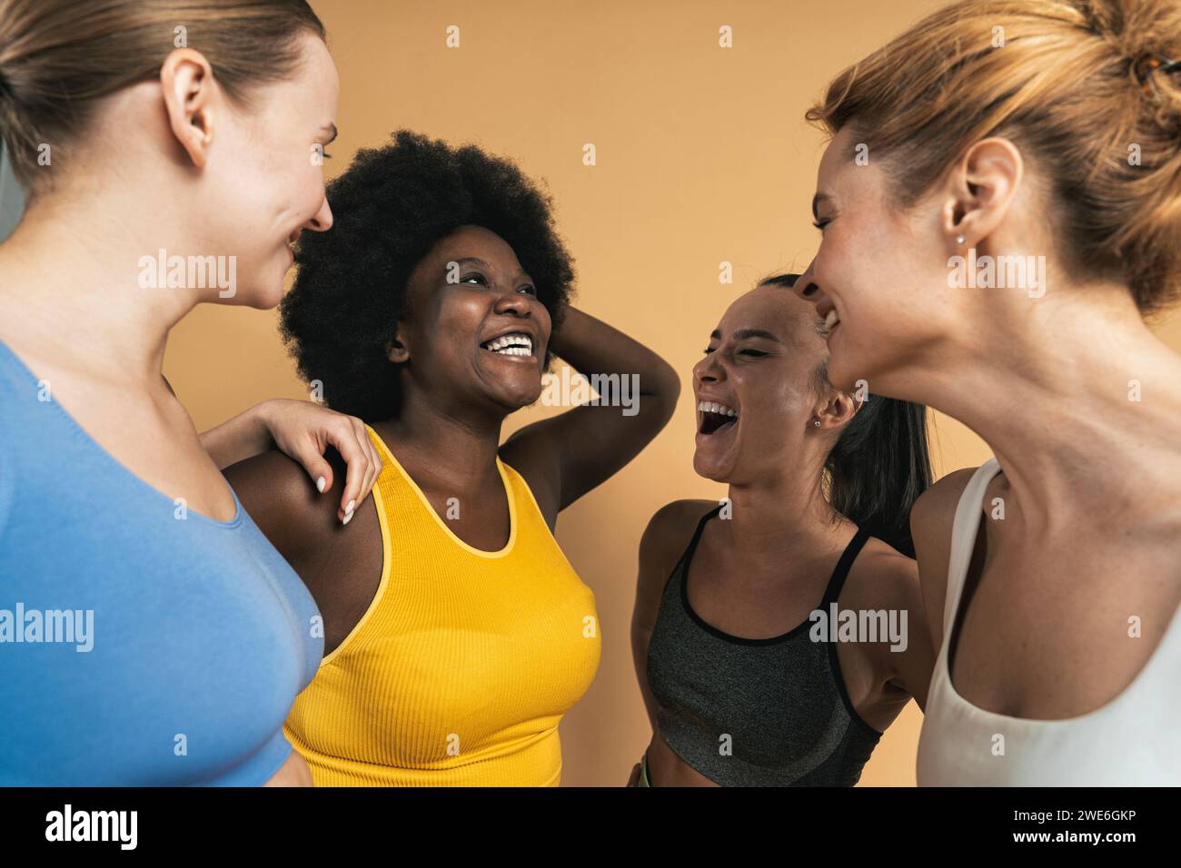 Allegri amici femminili multirazziali che ridono sullo sfondo beige Foto Stock