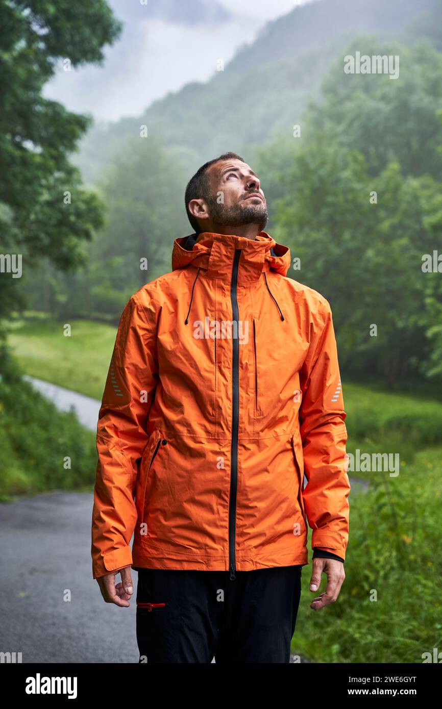 Uomo che indossa una giacca arancione e si trova di fronte alla montagna dei Pirenei Foto Stock