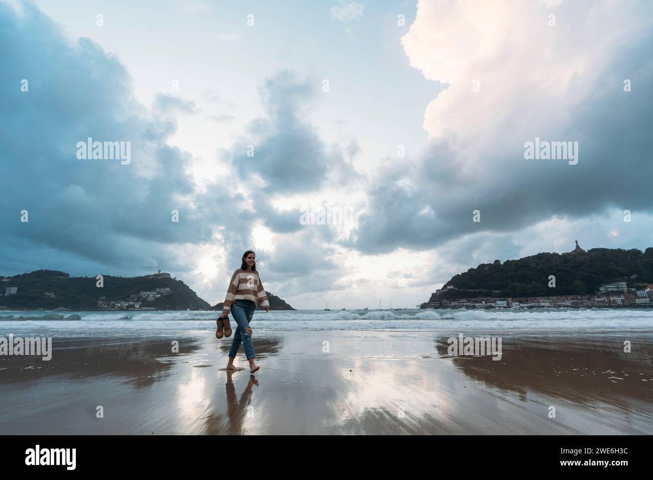 Giovane turista che cammina sulla spiaggia di Playa de la Concha al tramonto sotto il cielo nuvoloso Foto Stock