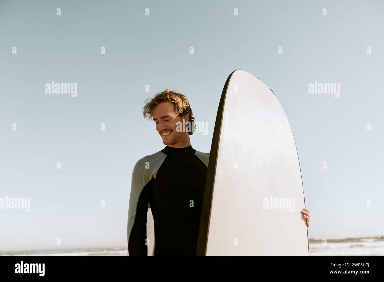 Surfista maschile in muta in piedi con la tavola da surf e si prepara a cavalcare sulle onde Foto Stock