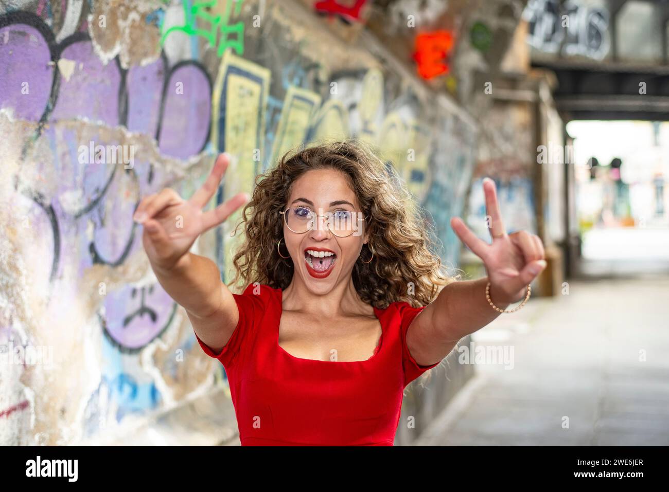 Donna allegra che gestisce il segno di pace vicino al muro dei graffiti sul sentiero Foto Stock