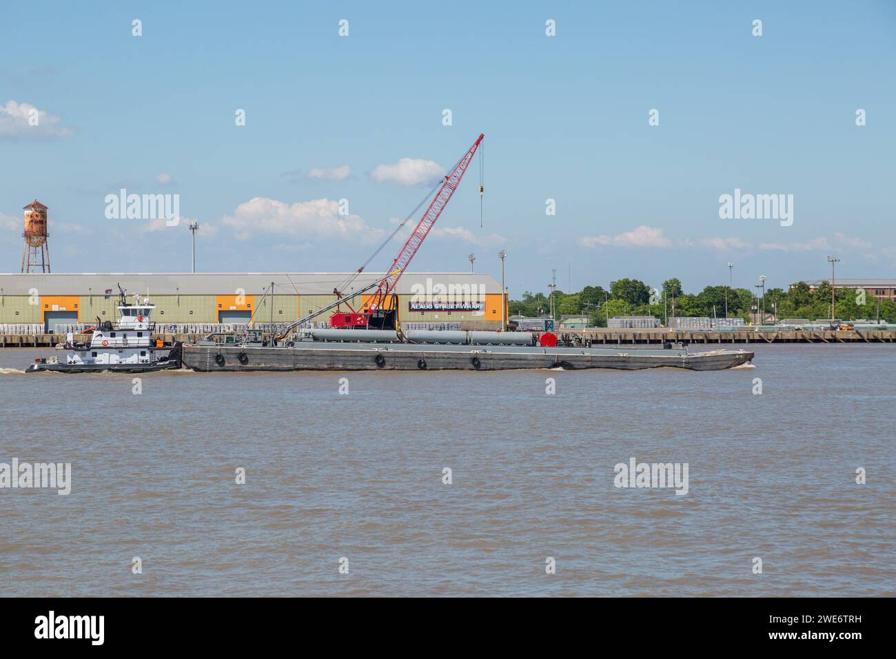Rimorchiatore Jennifer che spinge una grande chiatta con attrezzature da costruzione lungo il fiume Mississippi oltre l'Alabo Street Wharf a New Orleans, Louisiana Foto Stock