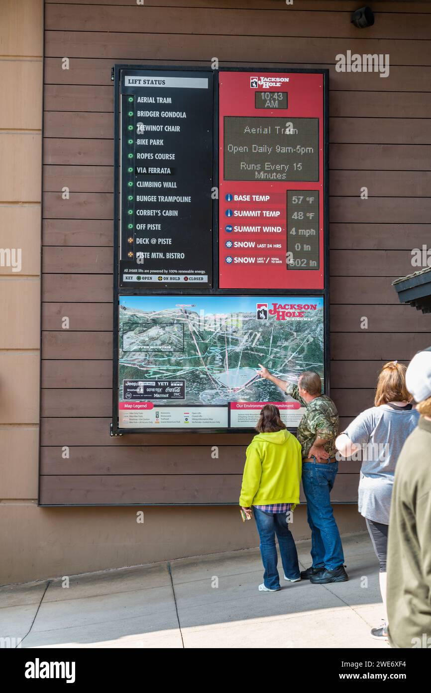 I turisti che guardano un cartello che mostra la mappa, le condizioni meteorologiche e lo stato degli ascensori Jackson Hole Aerial tram station a Teton Village, Jackson, Wyoming Foto Stock