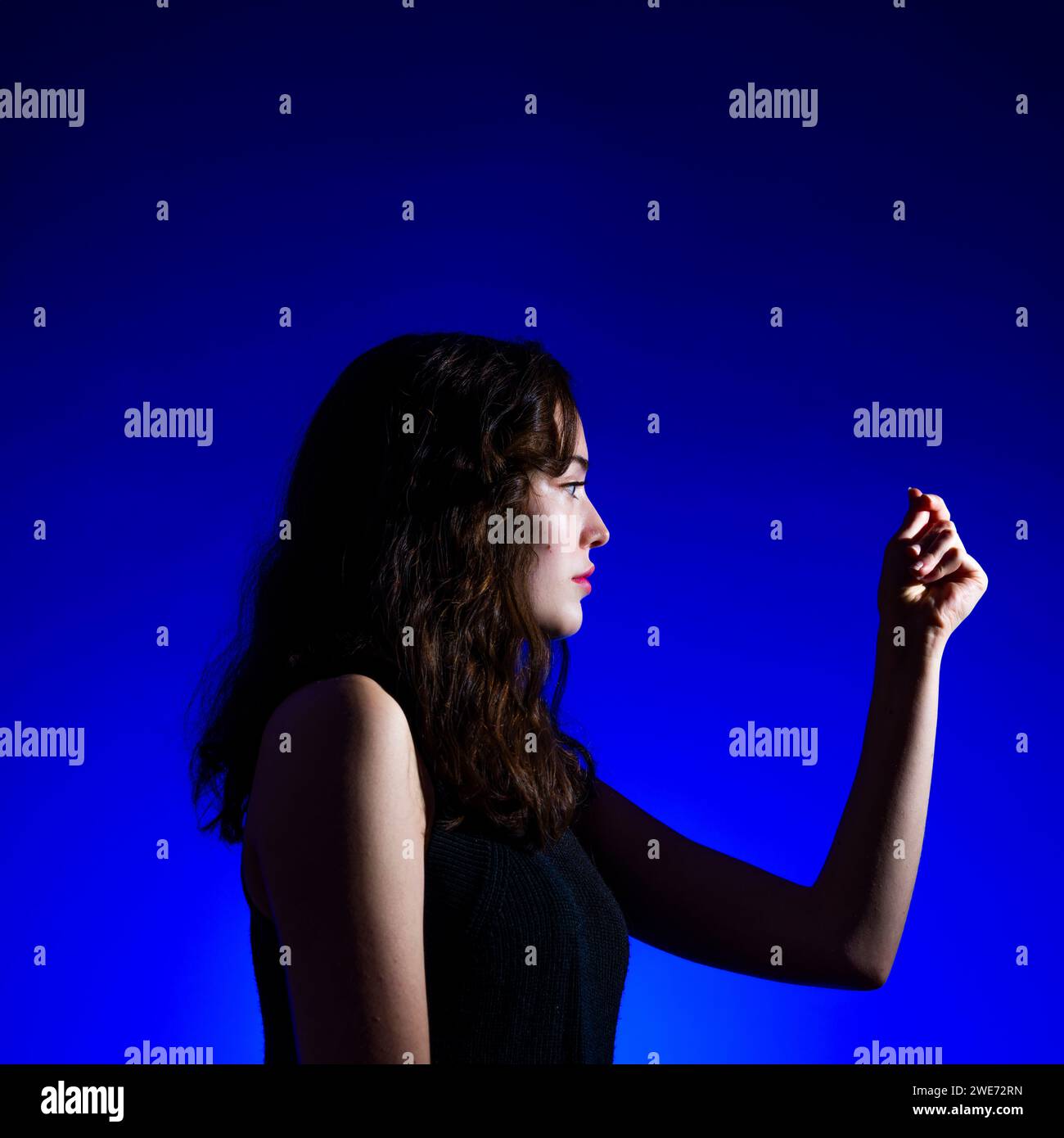 Bellissima ragazza adolescente che esamina la mano primo piano sfondo blu reale illuminazione Moody Copyspace Foto Stock