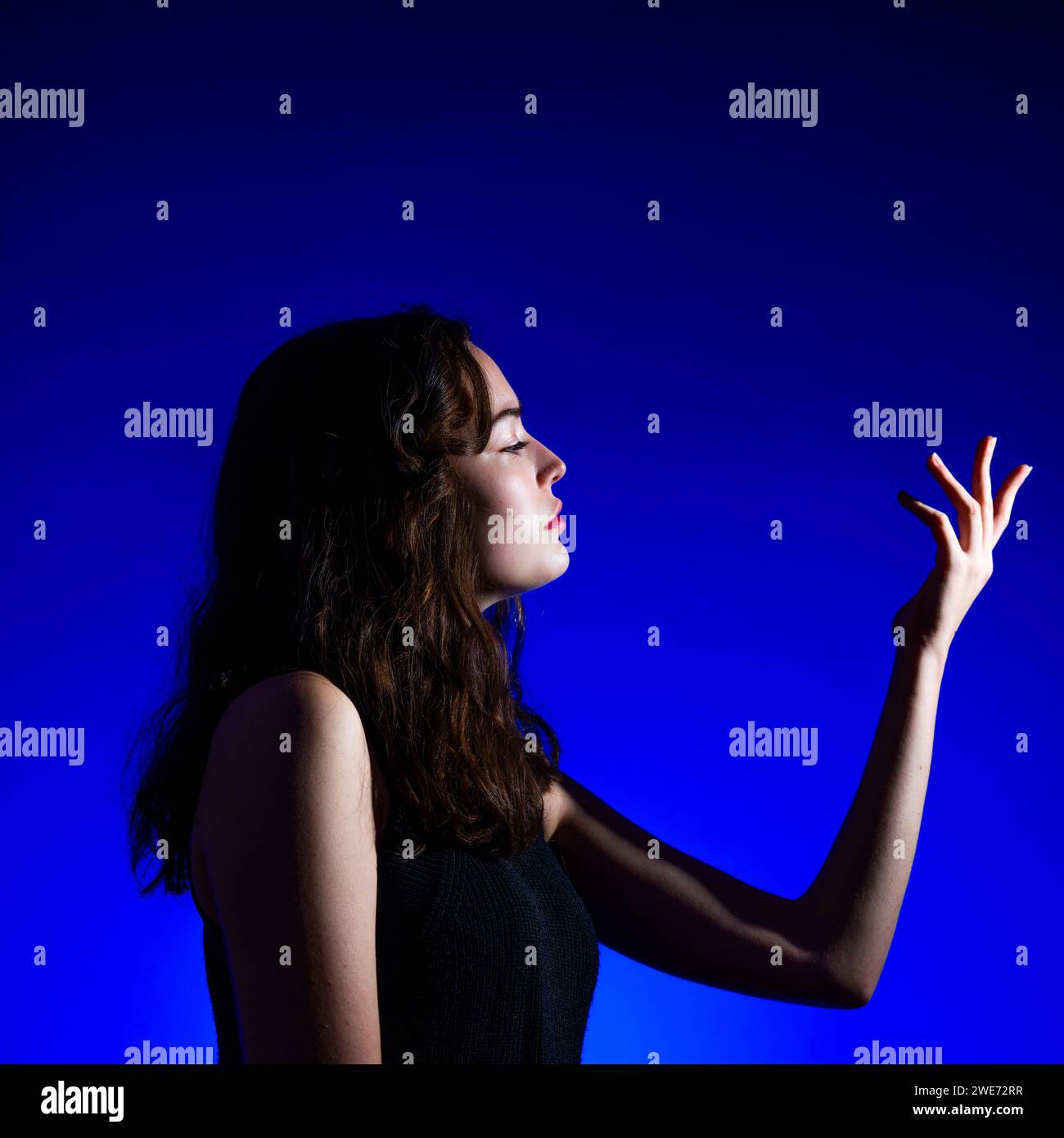 Bellissima ragazza adolescente che esamina la mano primo piano sfondo blu reale illuminazione Moody Copyspace Foto Stock