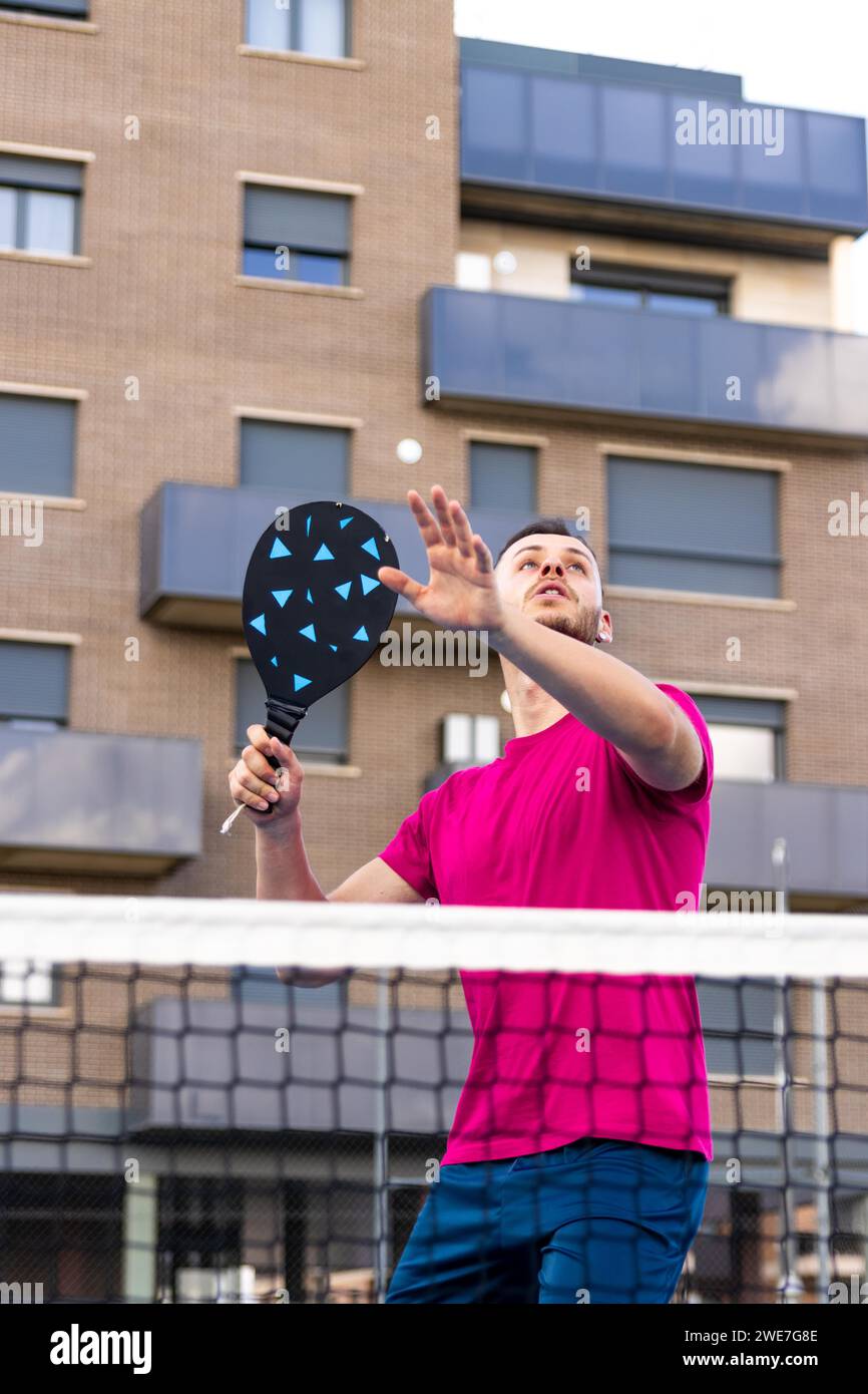 Uomo che si prepara a picchiare la palla in Pickleball. In Pickleball, è vietato il pallavolo (colpire la palla senza prima toccare il terreno) con qualsiasi Foto Stock