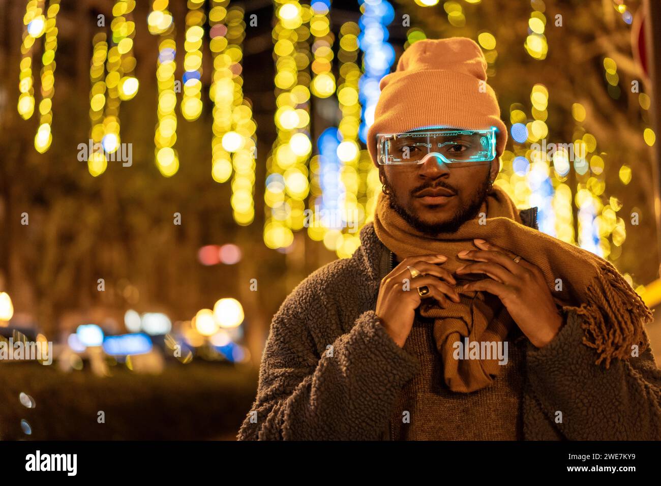 Uomo africano che indossa occhiali intelligenti in città di notte durante la vigilia di Natale Foto Stock