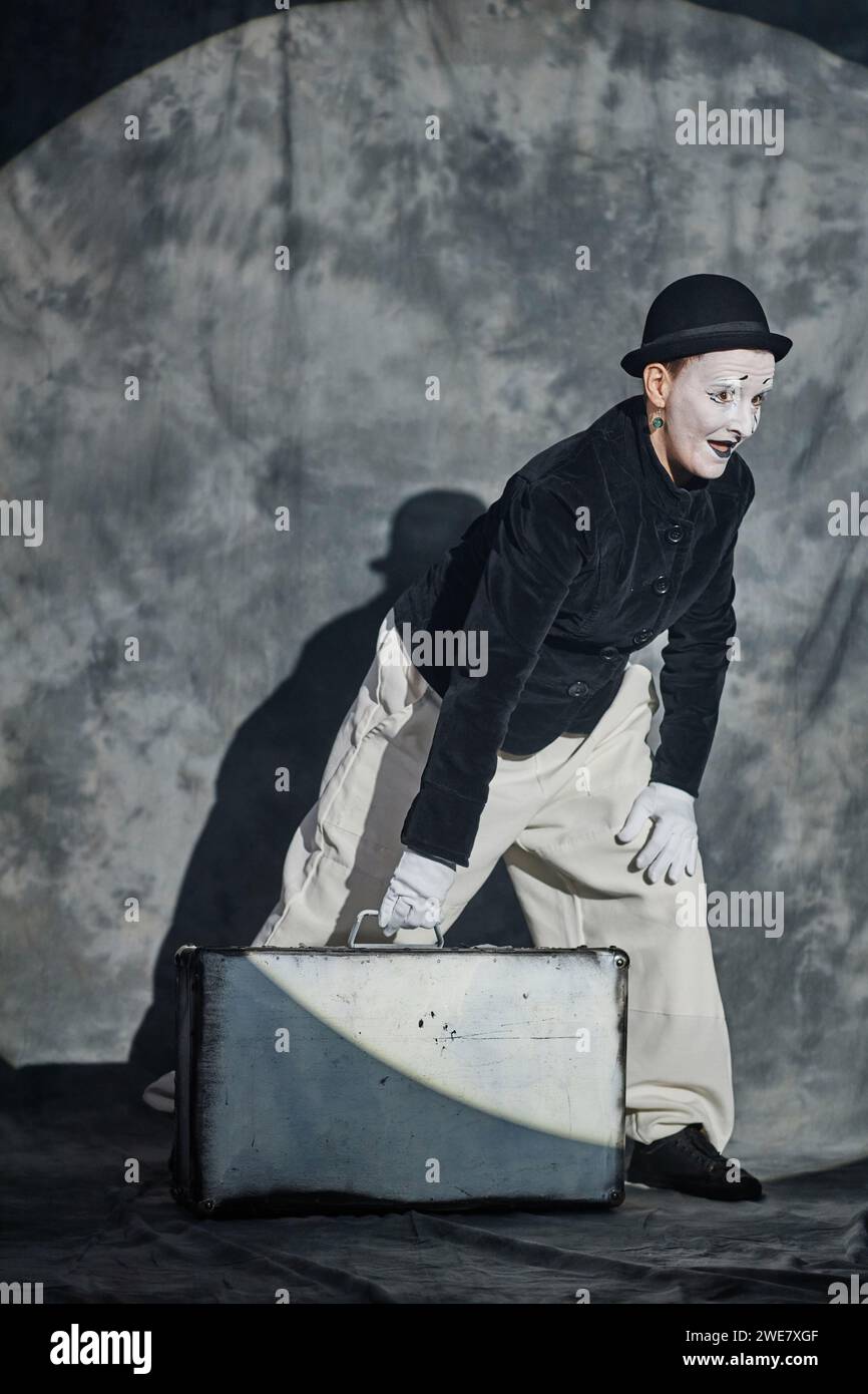 Ritratto verticale a tutta lunghezza di un artista mimo che si esibisce con una valigia sul palco sotto i riflettori Foto Stock