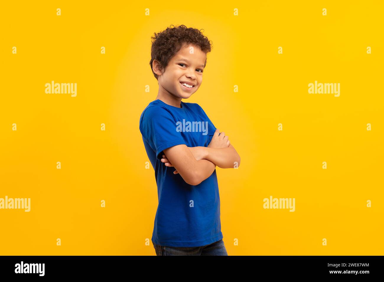 Ragazzo sicuro di sé con le braccia incrociate in camicia blu su sfondo giallo Foto Stock