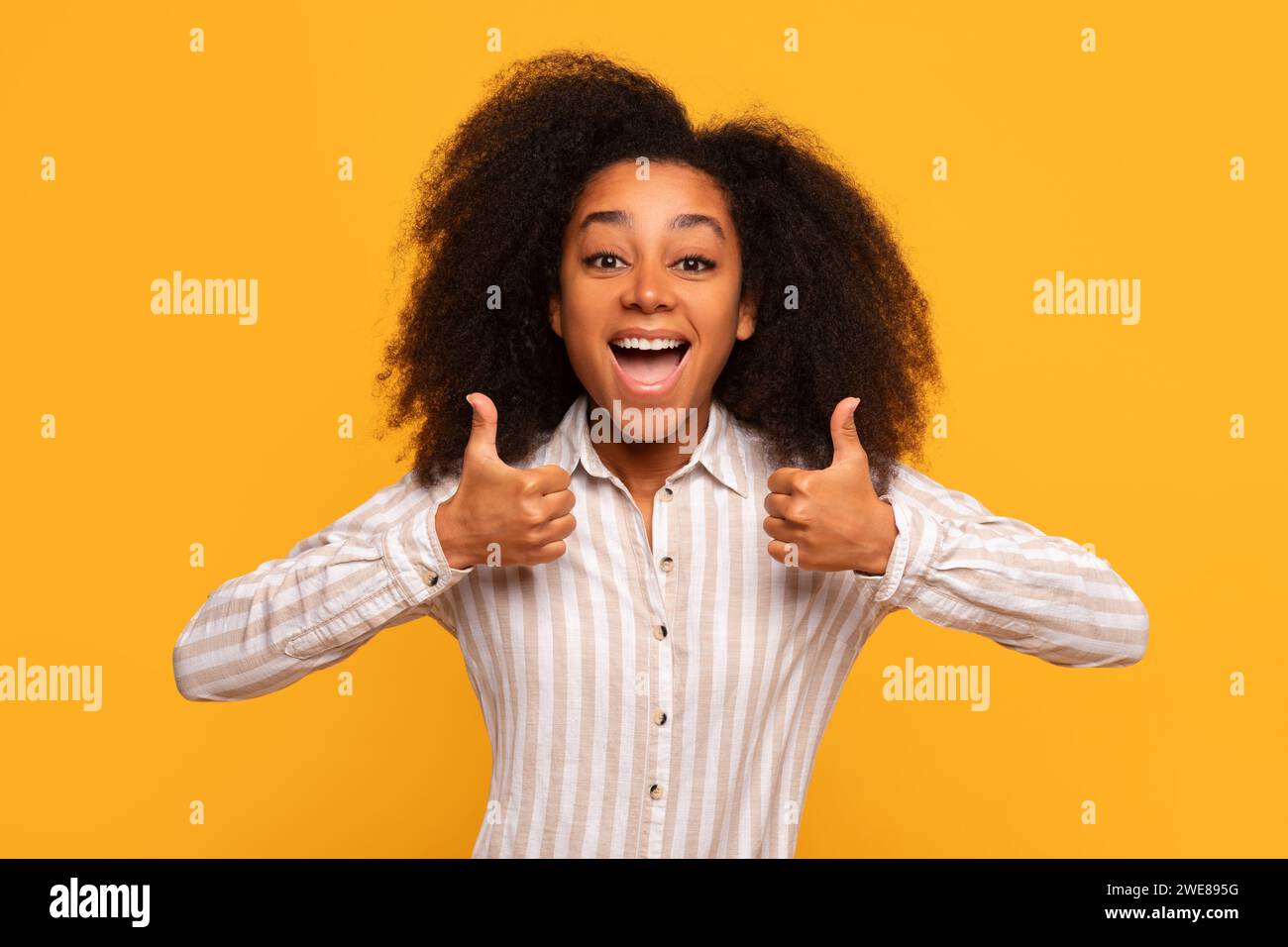Allegra donna nera che dà due pollici contro il muro giallo Foto Stock