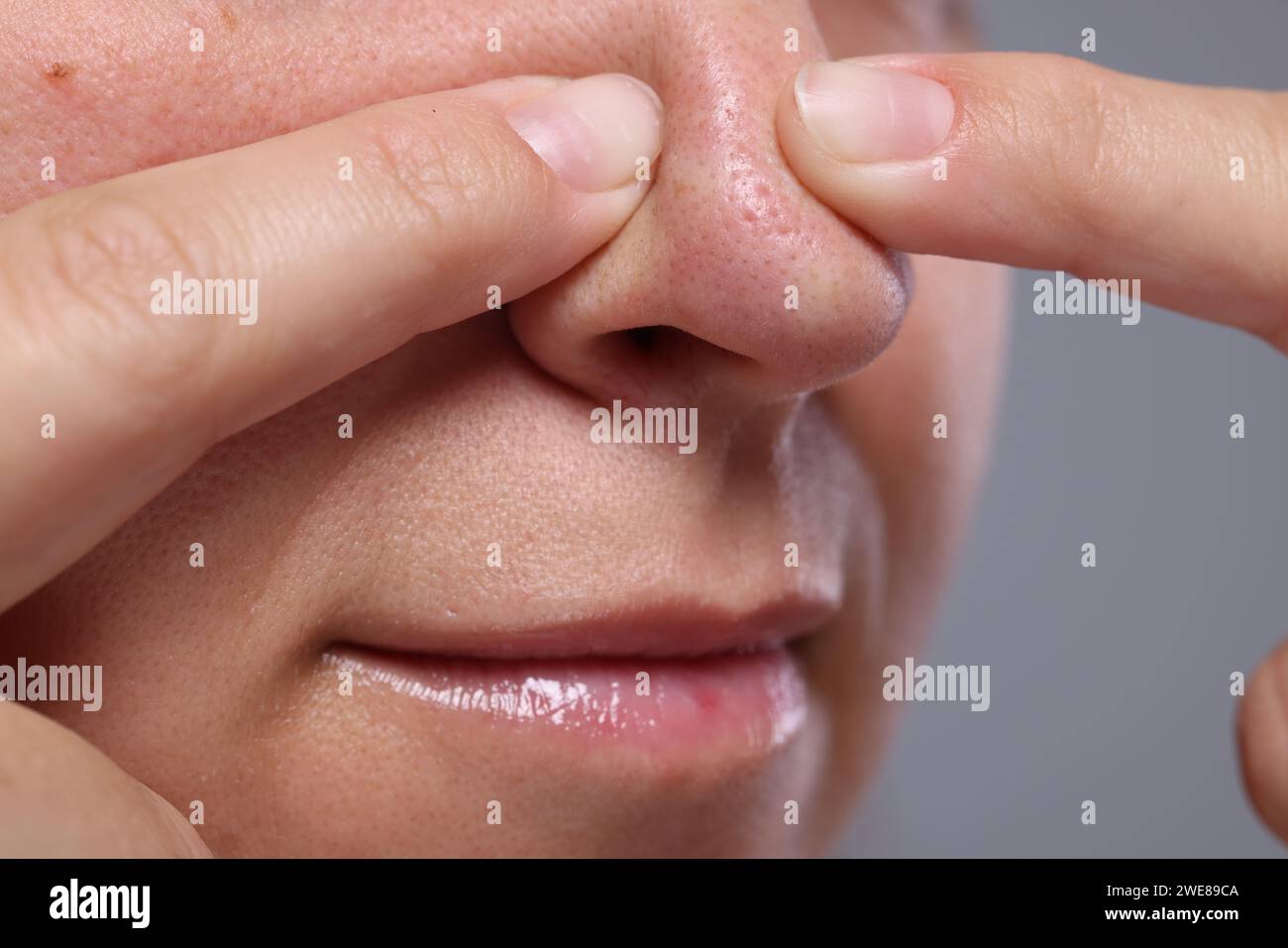 Donna che si fa scopare il naso su sfondo grigio, primo piano Foto Stock