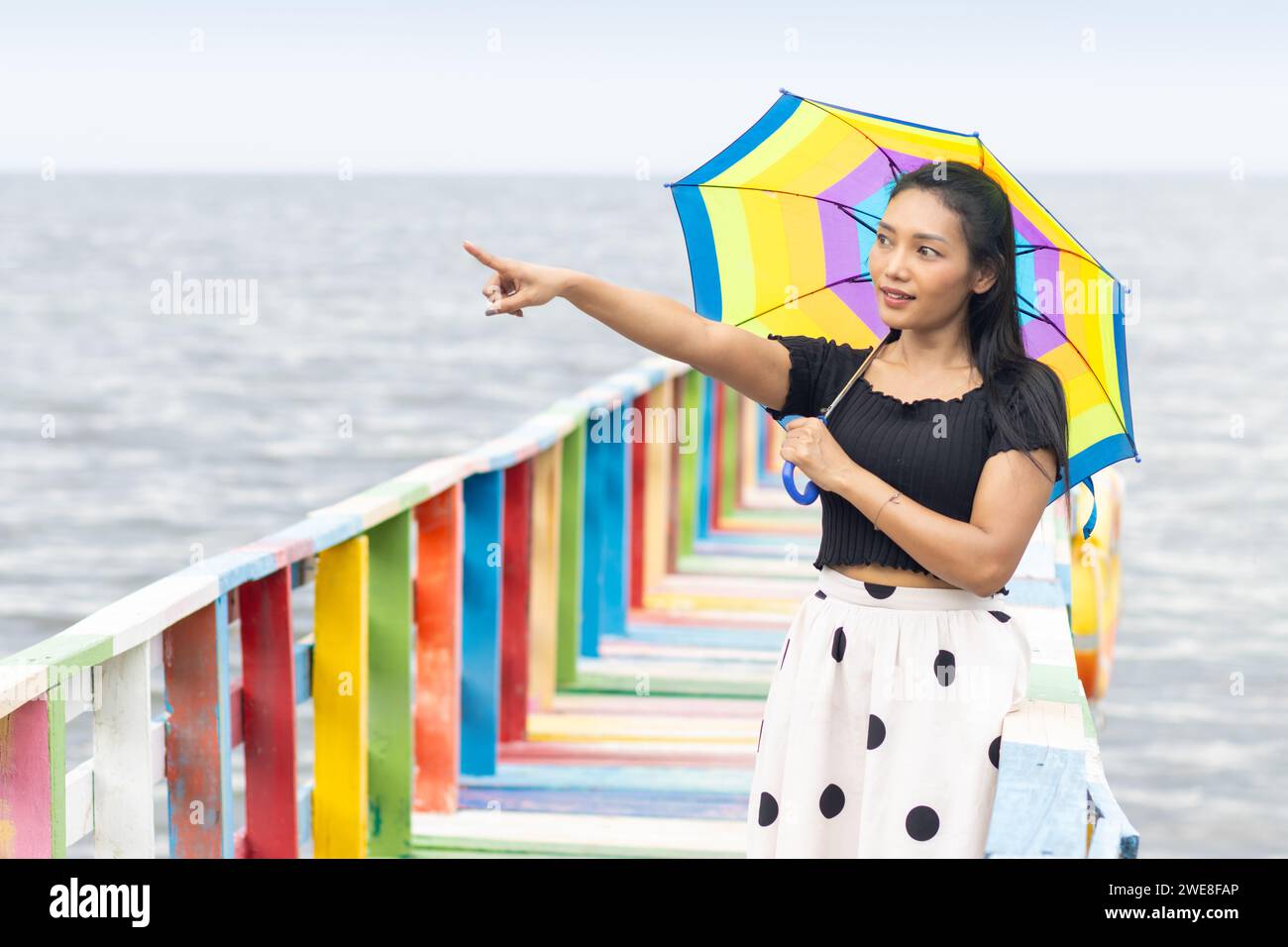 Una giovane donna con un ombrellone si trova sulla passerella colorata e punta con la mano Foto Stock