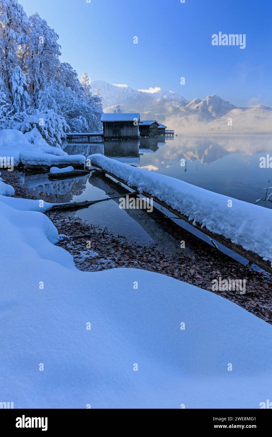 Boathouses, riflesso delle montagne nel lago, inverno, neve, sole, Lago Kochelsee, alta Baviera, Baviera, Germania, Europa Foto Stock