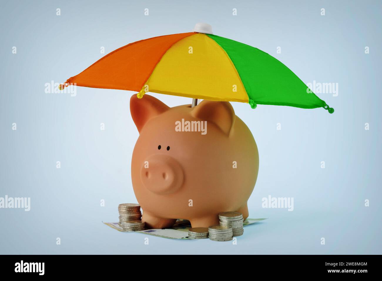 Salvadanaio con denaro sotto l'ombrello dell'arcobaleno - concetto di risparmio, protezione del denaro e sicurezza finanziaria Foto Stock