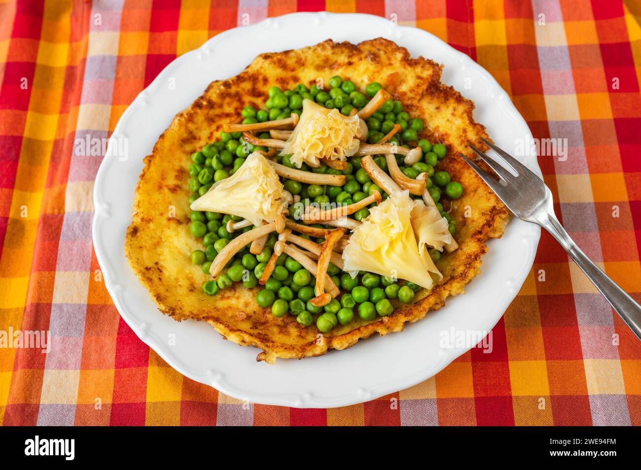 Omelette all'uovo con pisello bollito, funghi shimeji fritti e formaggio svizzero a forma di rosa su piatto bianco con forchetta su tovaglia a scacchi rosso-arancione e asciugamano. Foto Stock