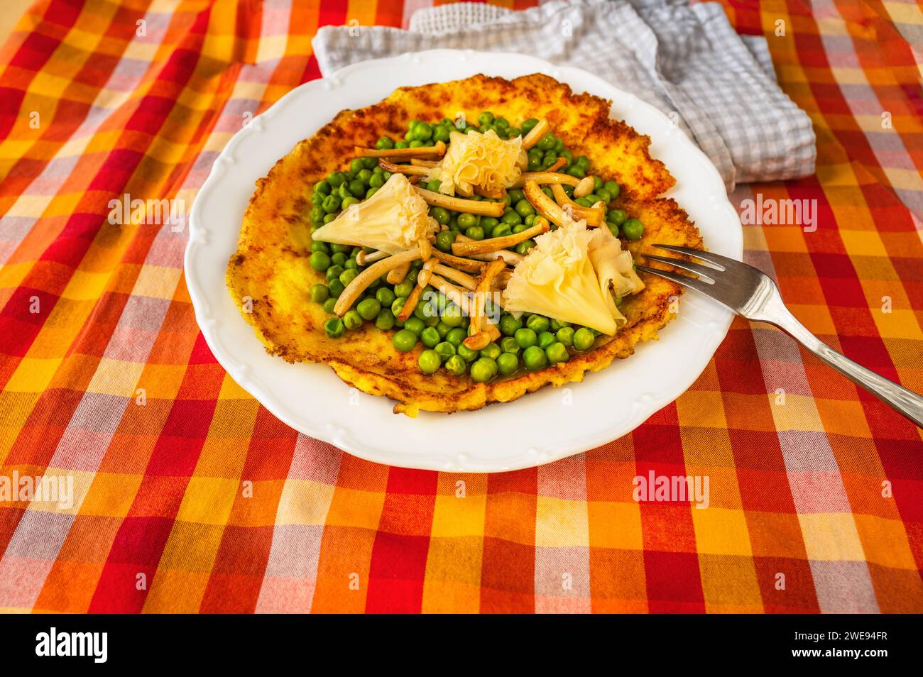 Frittata all'uovo con pisello bollito, fungo shimeji fritto e formaggio svizzero a forma di rosa su piatto bianco con forchetta su tovaglia a scacchi rosso-arancione, asciugamano, Foto Stock